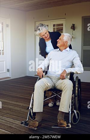 Taking care of each other in old age. a smiling senior man in a wheelchair and his wife outside their home. Stock Photo