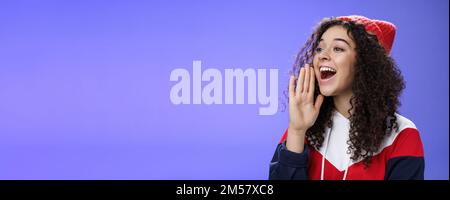 Friend shouting through street to turn attention. Portrait of carefree happy cute woman in beanie and sweatshirt holding palm near opened mouth Stock Photo