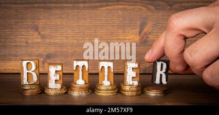 BETTER. Text from alphabet blocks and money on wood texture background. Stock Photo