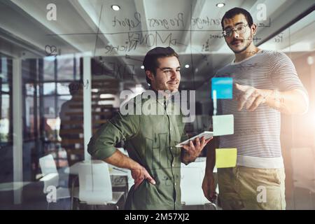 Sharing some ideas. two young designers planning on a glass board. Stock Photo