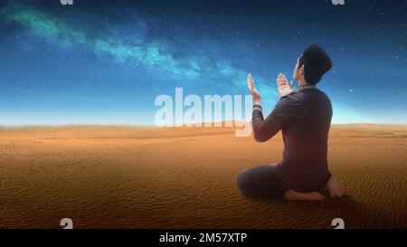 Muslim man sitting while raised hands and praying in the desert Stock Photo