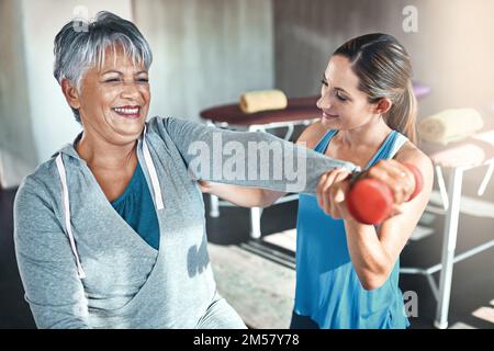 Get fit and have fun while doing it. a senior woman using weights and a fitness ball with the help of a physical therapist. Stock Photo