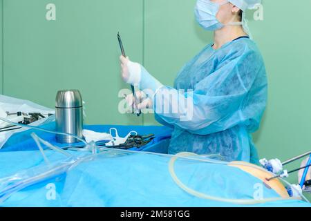 The doctor holds a sterile surgical instrument near the table in the operating room. Stock Photo
