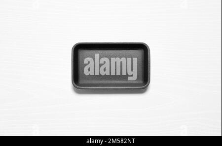 Black styrofoam tray against a white wood board from above Stock Photo