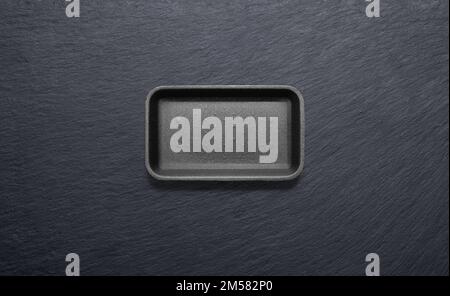 Black styrofoam tray against a black slate plate from above Stock Photo