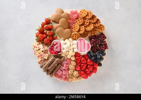 Charcuterie Valentines Day board with chocolate, red hearts, different sweets, strawberries, blueberries and candies on light gray background. View fr Stock Photo