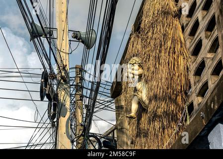 A cupid on a concrete block wall. A cupid on a wall with a heart-shape made of hay in the background, and messy electrical wires in the foreground. Stock Photo