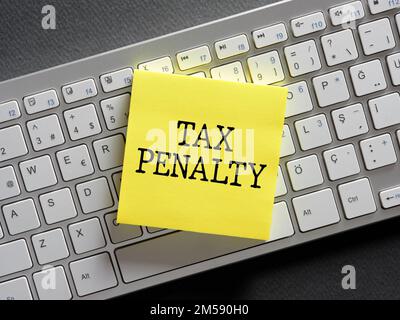The word tax penalty written on a sticky note paper on computer keyboard. Stock Photo