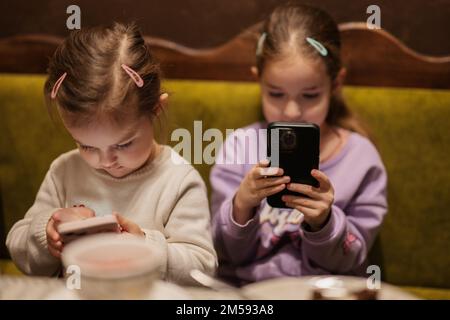 Sisters kids hold mobile phone together at cozy cafe and having fun. Stock Photo