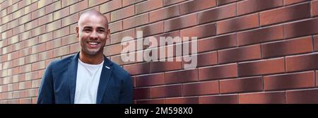 Positive emotion. Young guy standing leaning on wall looking aside smiling happy Stock Photo
