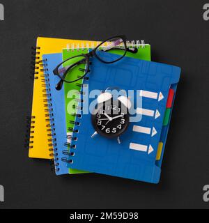 A stack of colored school notebooks and an alarm clock on a school chalkboard background. Back to school concept, banner Stock Photo