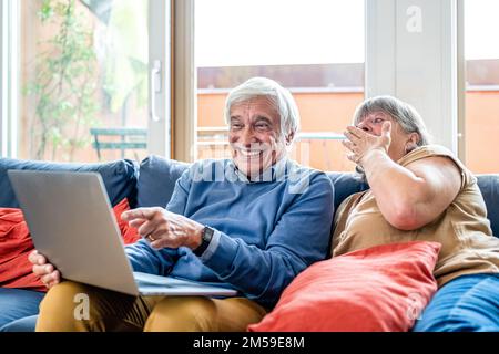 Couple senior using computer laptop on sofa at home for online shopping, surfing internet, elderly lifestyle and modern technologies Stock Photo