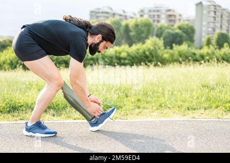 Young man with an artificial prosthesis replacing a leg prepares to train and fastens the straps of the artificial foot shoe, copy space Stock Photo