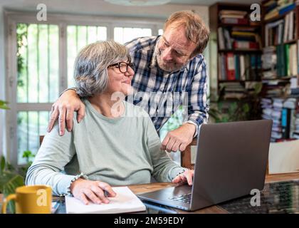 Embraced mature couple surfing the Internet on laptop at home, elderly lofstyle, senior people using laptop for shopping online Stock Photo