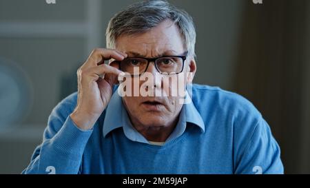 Close up portrait shocked old Caucasian businessman stressed upset man elderly 60s male worried holding head with shock fear take off eyeglasses Stock Photo