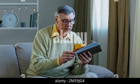 Old 60s elderly Caucasian man checking sorting letters in living room concentrated mature grandfather sitting on sofa looking at correspondence notice Stock Photo