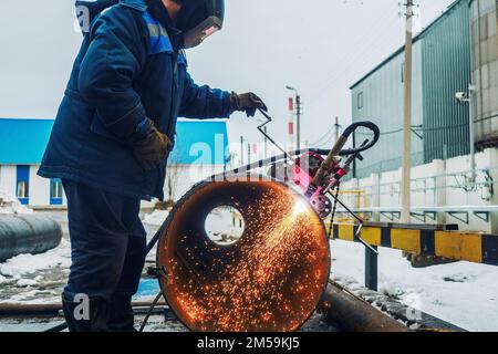 Working welder cuts metal and sparks fly. Gas cutting of large diameter pipes with acetylene and oxygen. Industrial metal cutting in oil and gas industry. Stock Photo