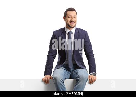 Man in jeans and suit sitting on a blank panel isolated on white background Stock Photo
