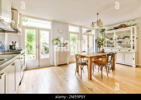 a kitchen and dining area in a house with wood flooring, white cabinets and wooden table surrounded by pots Stock Photo