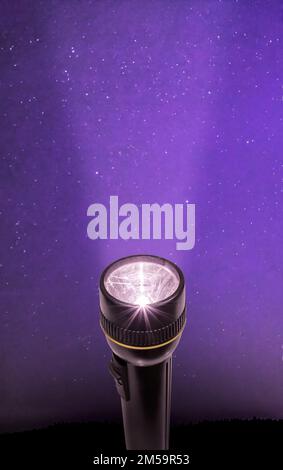 Flashlight sending a beam of light into a starry purple night sky. Stock Photo