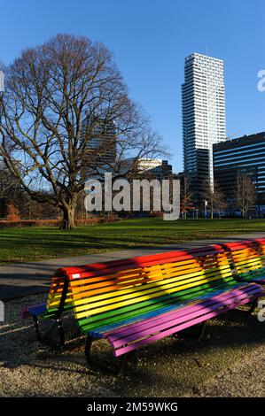 A vertical shot of an empty bench painted in rainbow colors in a public park Stock Photo
