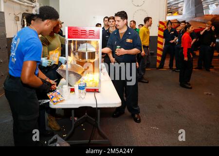 PHILIPPINE SEA (Feb. 14, 2022) Sailors line up for popcorn during a Super Bowl LVI viewing event in the hangar bay aboard the Nimitz-class aircraft carrier USS Abraham Lincoln (CVN 72). Abraham Lincoln Strike Group is on a scheduled deployment in the U.S. 7th Fleet area of operations to enhance interoperability through alliances and partnerships while serving as a ready-response force in support of a free and open Indo-Pacific region. Stock Photo