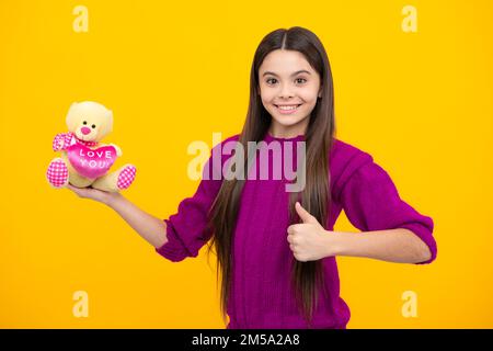 Teen girl child in casual wear holding plush toy isolated on yellow background, happy childhood. Stock Photo