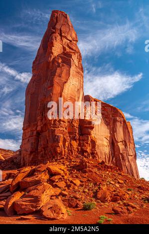 A large monolithic stone stands high overhead against a brilliant blue summer sky with 'angels wings' in Monument Valley, Arizona. Stock Photo