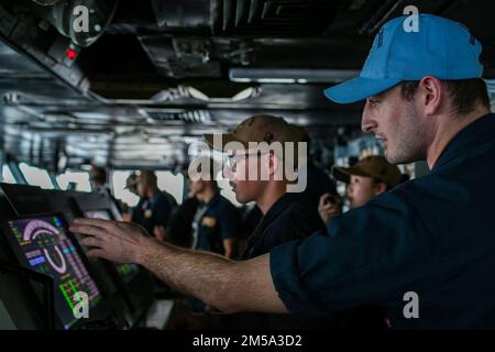 PHILIPPINE SEA (Feb. 14, 2022) Quartermaster 2nd Class Steven Pettit, right, a master helmsman, from Ionia, Mich., gives instruction to a helmsman, Seaman Jacob Bender, from Columbus, Ohio, on the bridge aboard the Nimitz-class aircraft carrier USS Abraham Lincoln (CVN 72). Abraham Lincoln Strike Group is on a scheduled deployment in the U.S. 7th Fleet area of operations to enhance interoperability through alliances and partnerships while serving as a ready-response force in support of a free and open Indo-Pacific region. Stock Photo