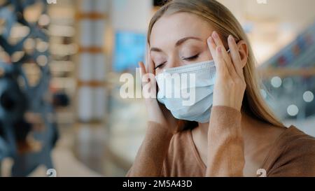 Caucasian lady sick suffering blonde girl ill woman wearing medical mask holding temples forehead feeling fear flu virus symptoms coronavirus pandemic Stock Photo