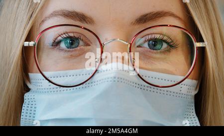 Extreme close up female face Caucasian girl woman with blue eyes wear glasses and medical mask female doctor nurse lab worker in respirator and Stock Photo