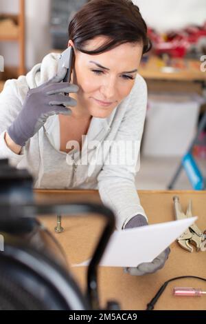 female technician making call on smartphone in the workshop Stock Photo