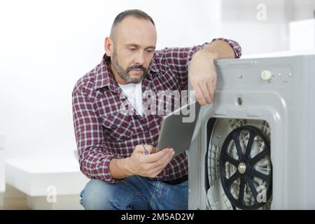 man using tablet to fix a washing machine Stock Photo