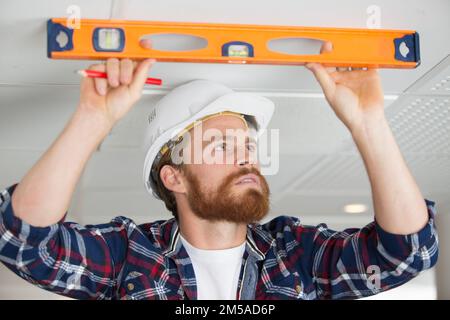 male construction worker holding spirit level against ceiling Stock Photo