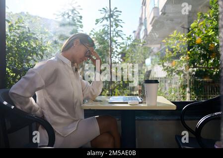 Tired stressed woman suffering from neckpain working from home office sitting at table. Overworked young aged lady massaging neck feeling hurt pain Stock Photo