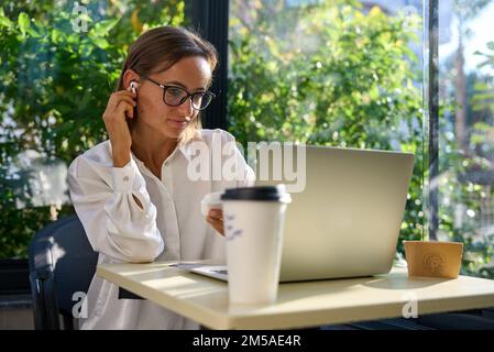 Young woman on video call using laptop. Happy businesswoman having a virtual meeting with a client in a cafe Stock Photo
