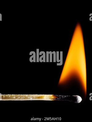 A lit wooden match burns with an orange flame against a black background Stock Photo