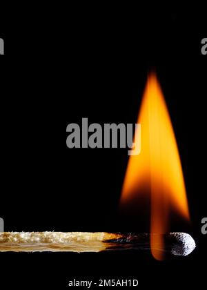 A lit wooden match burns with an orange flame isolated on black background Stock Photo