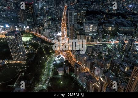 An aerial view of long exposure of lights of the traffic on the star-shaped road loops in the downtown of Tokyo, with a cityscape at night Stock Photo