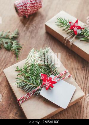 Christmas DIY presents wrapped in craft paper with fir tree twigs. Red decorations in shape of Christmas tree, stars. New Year gifts on wooden backgro Stock Photo