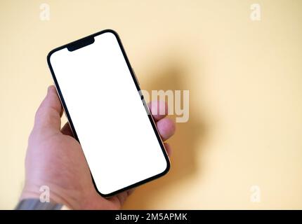 Hand holding black smartphone isolated on yellow background, white screen background. Hand holding a smartphone with green screen, empty, copy space. Stock Photo