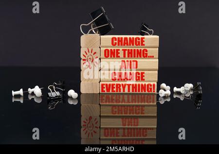 Business concept. On a black reflective surface are buttons, clips and wooden blocks with the inscription - Change One Thing... and Change Everything Stock Photo