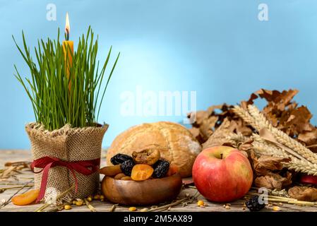 Traditional food for orthodox Christmas eve. Yule log or badnjak, apples, bread, cereals, dried fruit and a burning candle in green wheat on a wooden Stock Photo