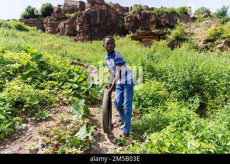 Cute African boy playing alone with an old tire letting it roll down the hill on a dirt path Stock Photo