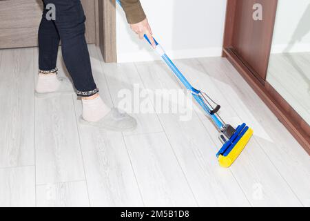 A woman washes the laminate floor in the apartment with a mop. House cleaning. Stock Photo