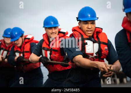 SOUTH CHINA SEA (Feb. 18, 2022) Yeoman Seaman Christopher Davis, right, from Selma, Alabama, and other Sailors assigned to the Arleigh Burke-class guided-missile destroyer USS Dewey (DDG 105) pull in the messenger line during a replenishment-at-sea with the Military Sealift Command dry cargo and ammunition ship USNS Amelia Earhart (T-AKE 6). Dewey is assigned to Destroyer Squadron (DESRON) 15 and is underway supporting a free and open Indo-Pacific. CTF 71/DESRON 15 is the Navy’s largest forward-deployed DESRON and the U.S. 7th Fleet’s principal surface force. Stock Photo