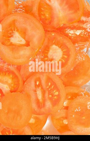 Close-up fresh slices of tomato on white background. Slices of tomato in sparkling water on white background, close-up. Vertical image Stock Photo