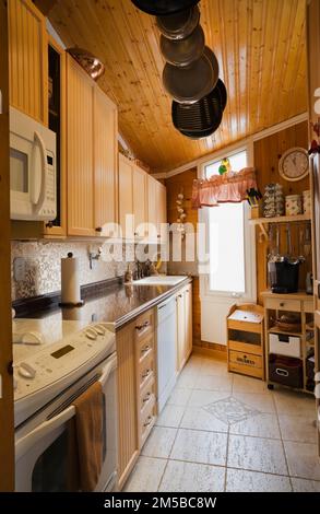 Bleached maple wood cabinets, pine wood plank wall and ceiling, travertine ceramic tile floor in kitchen inside 1987 Archimed style home. Stock Photo