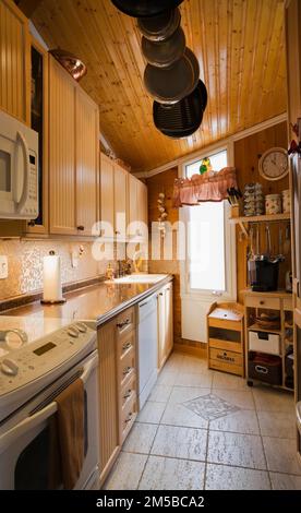 Bleached maple wood cabinets, pine wood plank wall and ceiling, travertine ceramic tile floor in kitchen inside 1987 Archimed style home. Stock Photo