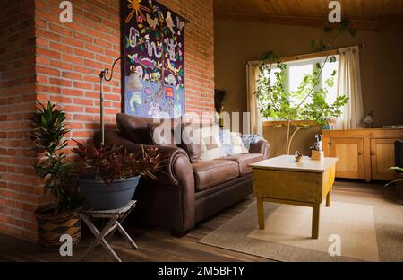 Brown leather sofa against red brick wall and antique wooden coffee table in living room on upstairs floor inside country cottage style log home. Stock Photo